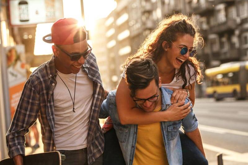 Three friends laughing together on a city street, showing how emotional numbness can hide behind outward smiles.