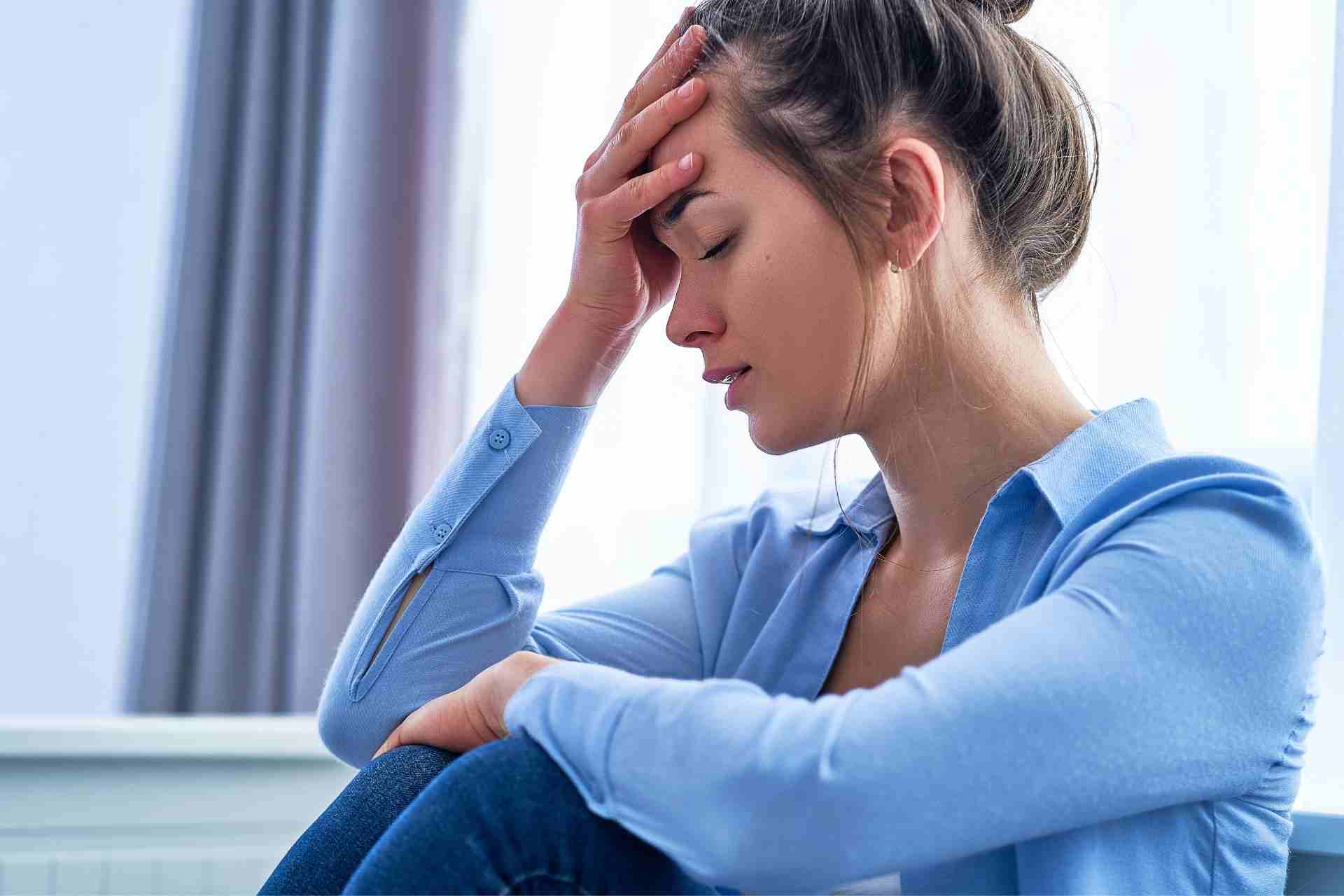 Woman sitting with her hand on her forehead, showing emotional exhaustion and symptoms of high-functioning depression.