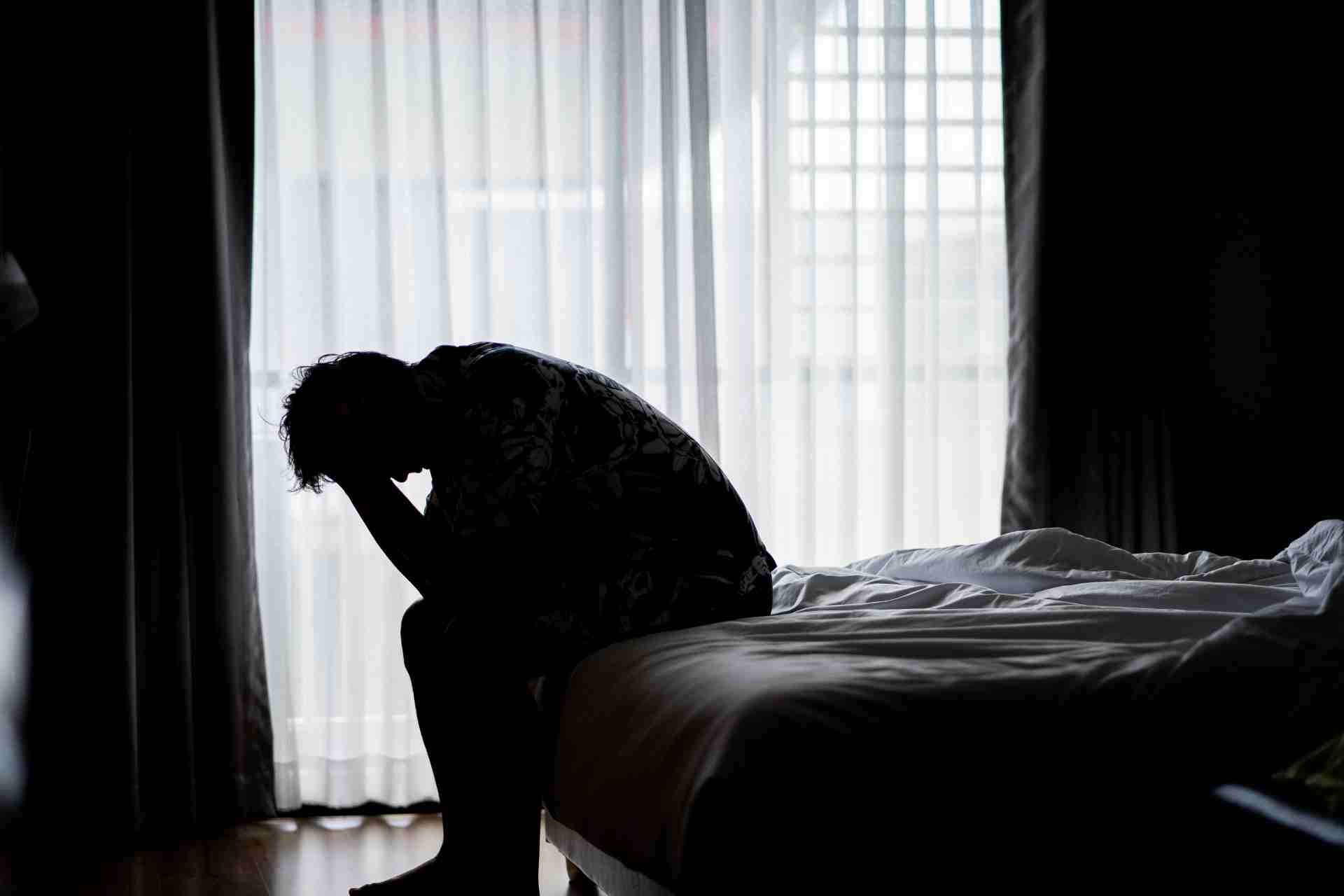 Silhouette of a person sitting on a bed with head in hands showing the emotional impact of severe depression