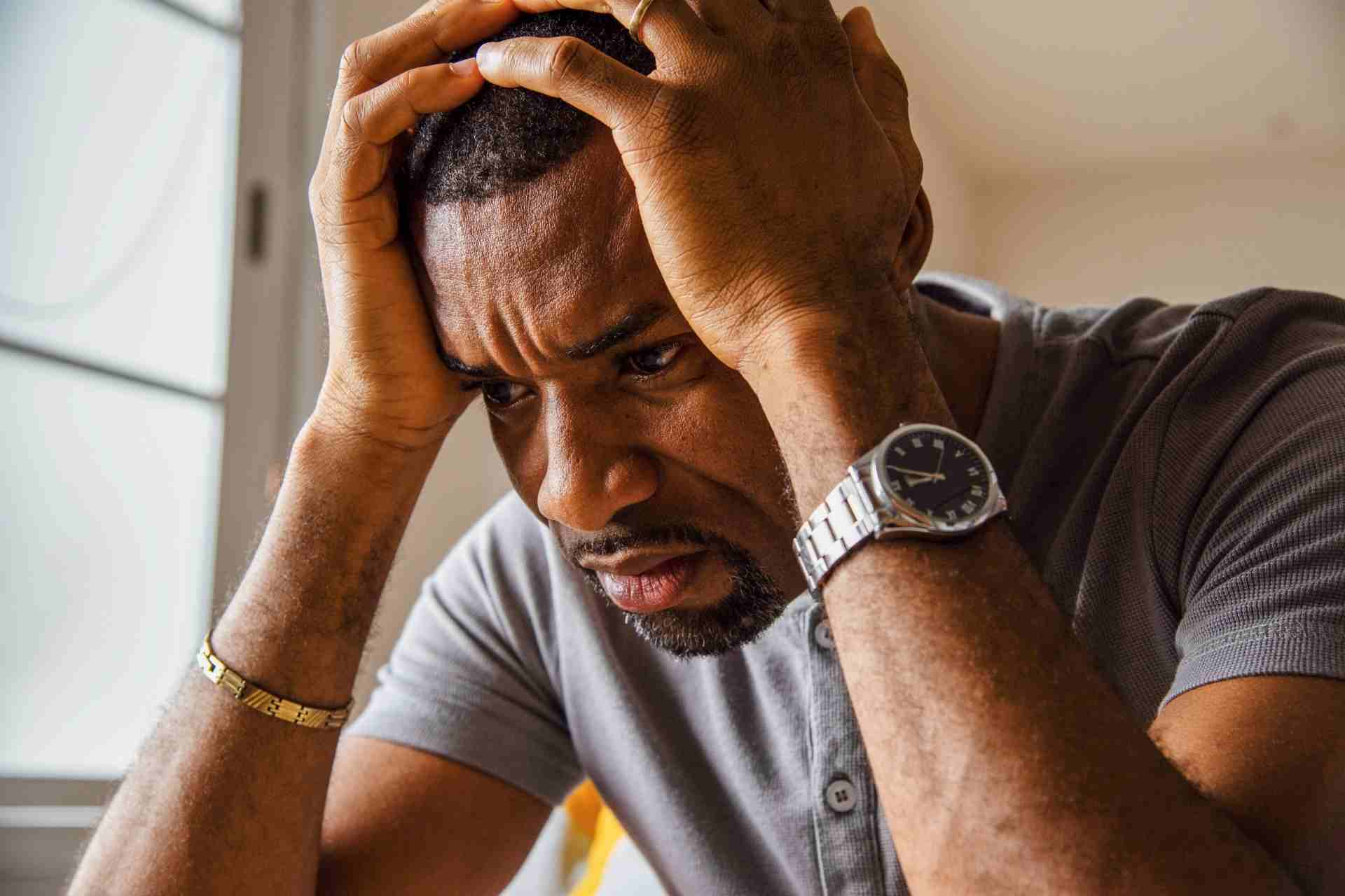 Man experiencing emotional distress and symptoms of trauma while holding his head in frustration.