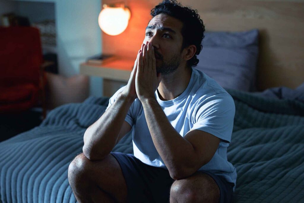 Man sitting on the edge of a bed while experiencing grief and emotional distress.