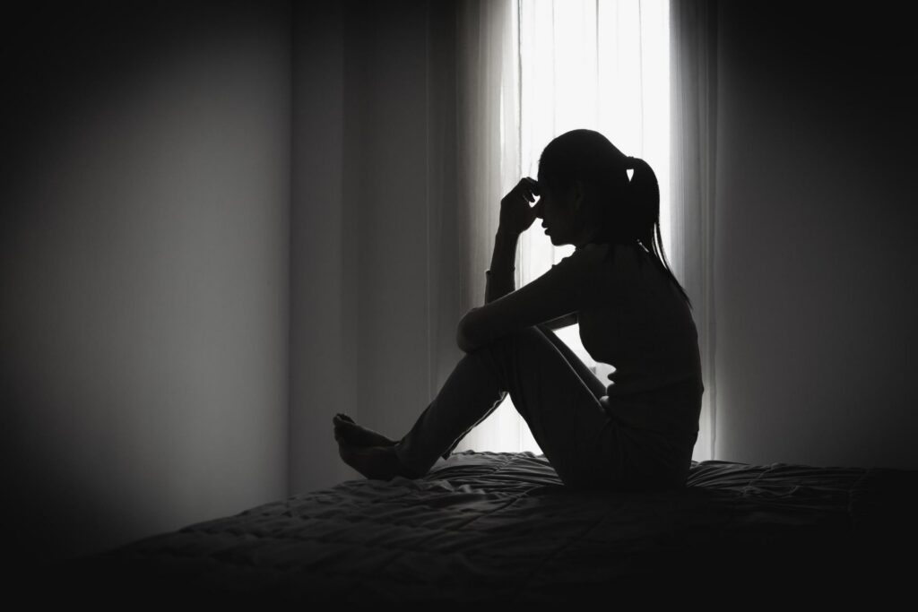 Woman sitting alone by a window while experiencing emotional stress